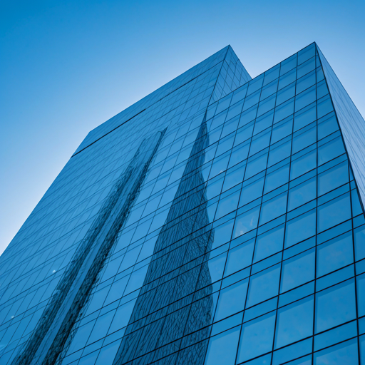 Modern glass skyscraper reflecting a clear blue sky at dawn.